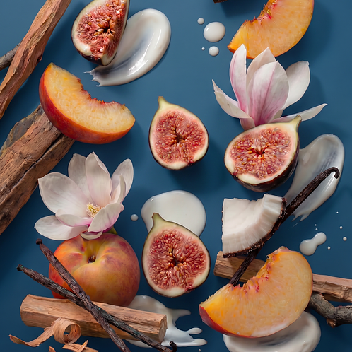 A flat lay arrangement of raw ingredients for Solace fine fragrance on a slate blue background, featuring sliced fresh figs, peach halves and slices, white magnolia blossoms, vanilla beans, sandalwood sticks, and swirls of white cream.