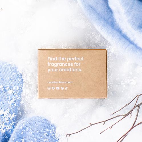 A kraft fragrance flight box on a snowy background with light blue mittens. 