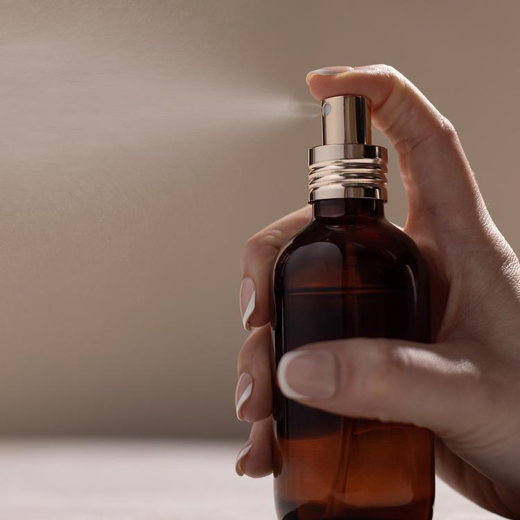 An elegant amber perfume bottle with a soft gold top spraying perfume