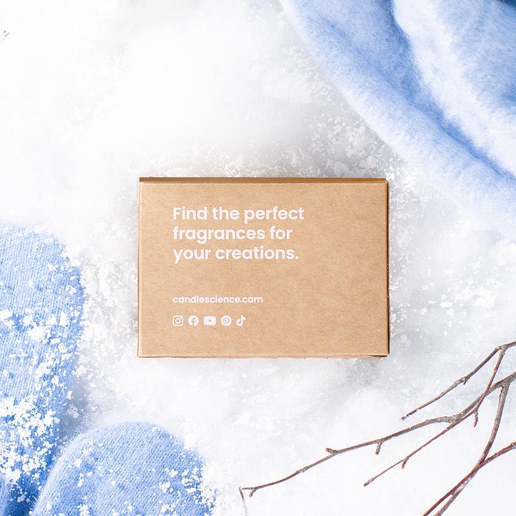 A kraft fragrance flight box on a snowy background with light blue mittens. 