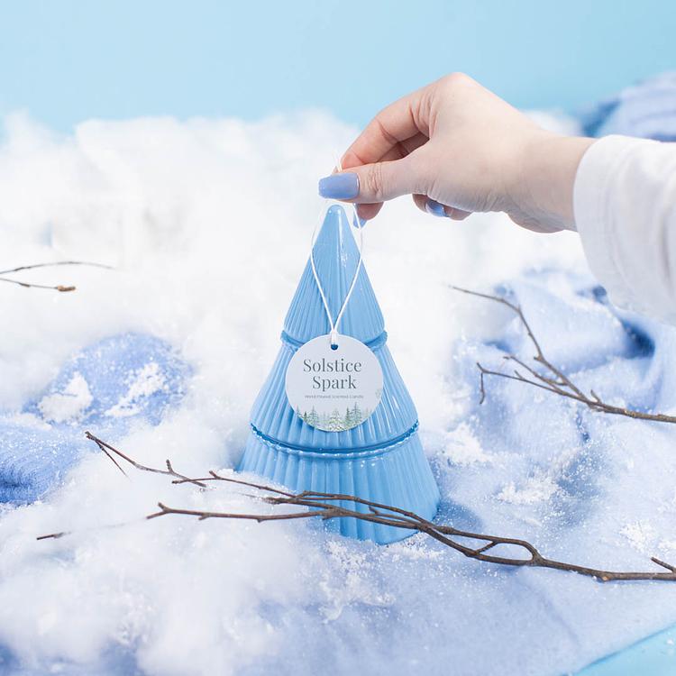 Ice Blue Tiered Glass Tree Jar on a blue and white icy backdrop with a hand lifting off the top layer of the candle