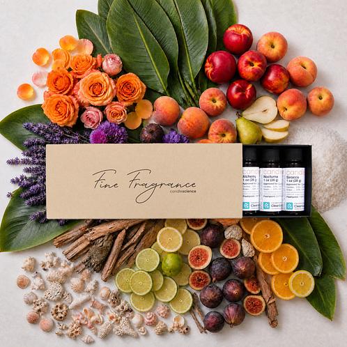 A gorgeous photo of a Fine Fragrance Sampler box holding eight 1 oz fragrance oils. The background is composed of roses, banana leaves, apple slices, sea salt, figs, and an assortment of items representing the fragrances. 