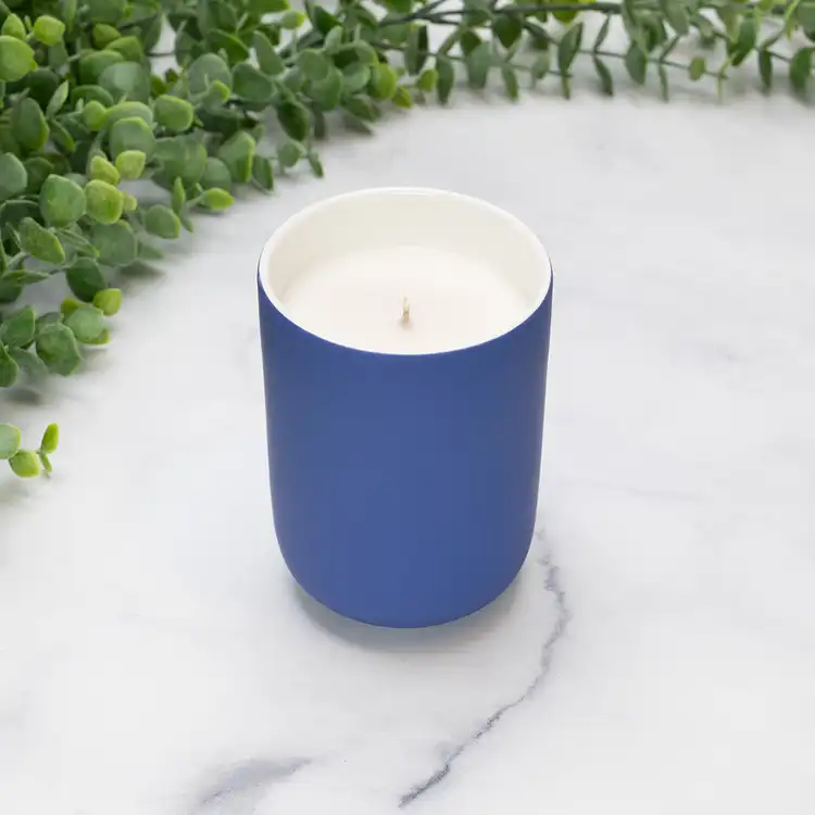 Blue Iris Dream Ceramic Tumbler Jar Candle in front of greenery