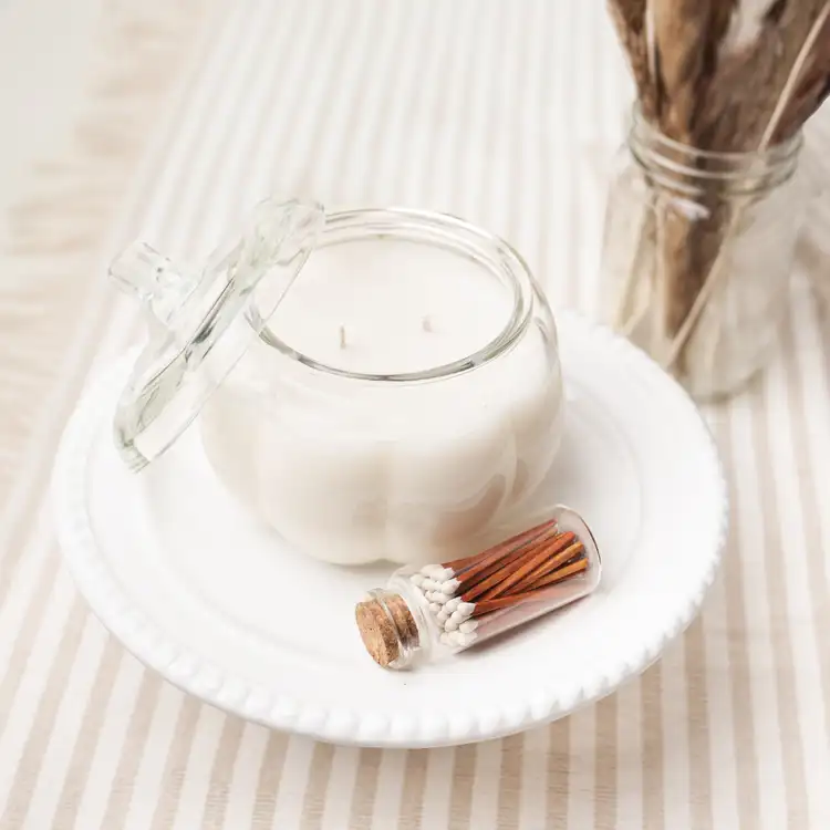 Clear Pumpkin Jar with the lid on its side is filled with a white wax candle. A bottle of matches sits beside it.