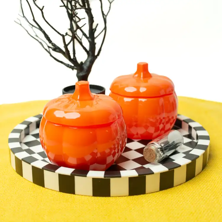 Two orange pumpkin jars on a black and white checkered tablecloth with a spooky tree.