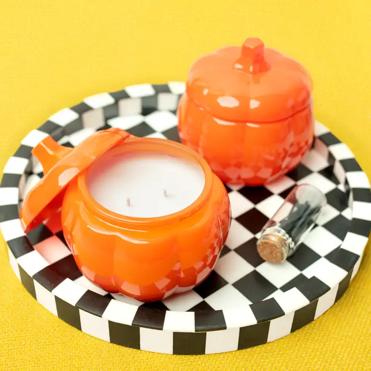 Two orange pumpkin jars on a black and white checkered tablecloth.