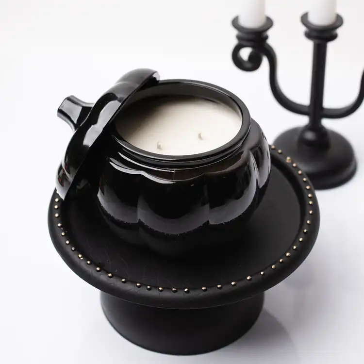 A black pumpkin jar with stem lid with a candelabra and lid on its side