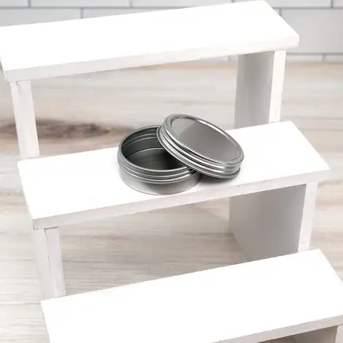 1 oz. Flat Tin with Screw Top Lid with lid off on riser