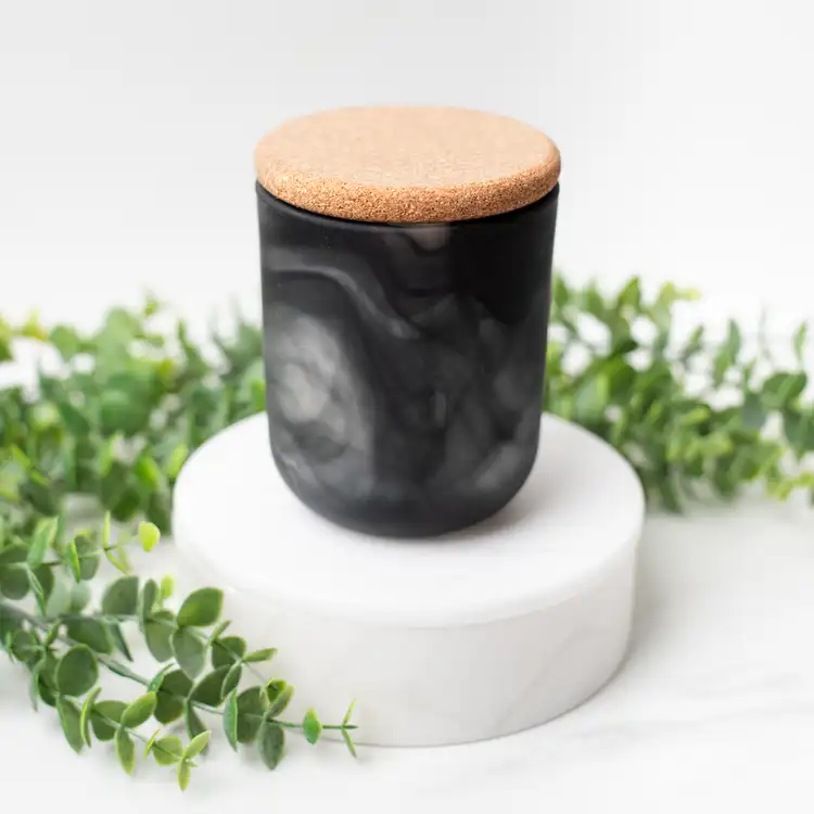 Frosted Black Swirl Sonoma Tumbler with a Rounded Cork Lid on a white marble podium surrounded by ivy with a black background.