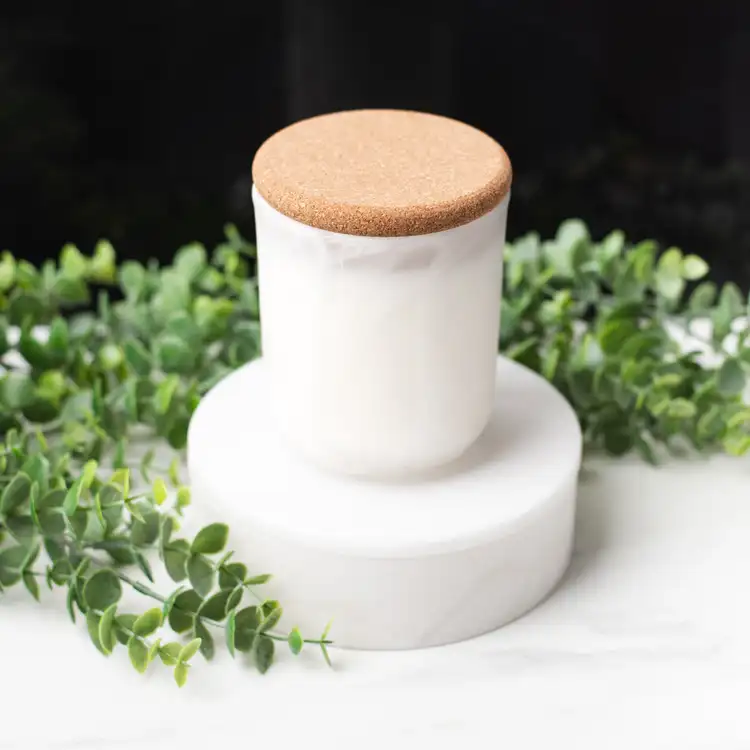 Frosted White Swirl Sonoma Tumbler with a Rounded Cork Lid on a white marble podium surrounded by ivy with a black background.