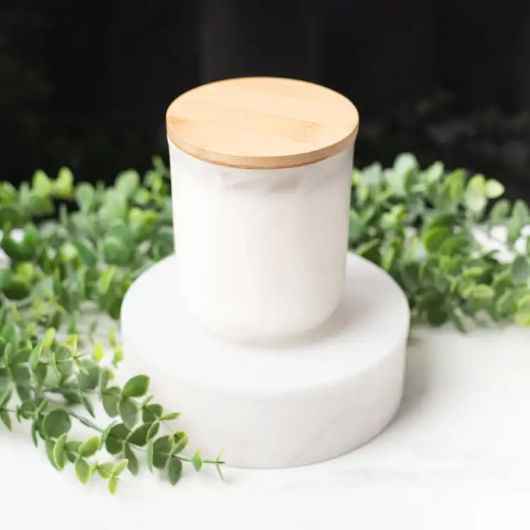 Frosted White Swirl Sonoma Tumbler with a Bamboo Lid on a white marble podium surrounded by ivy with a black background.