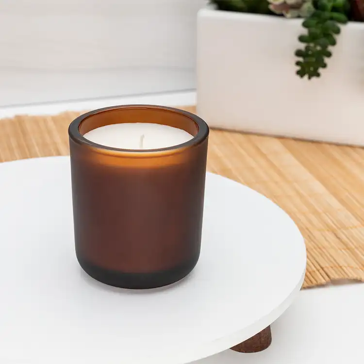 Mini Frosted Amber Sonoma Tumbler Jar candle in front of plants