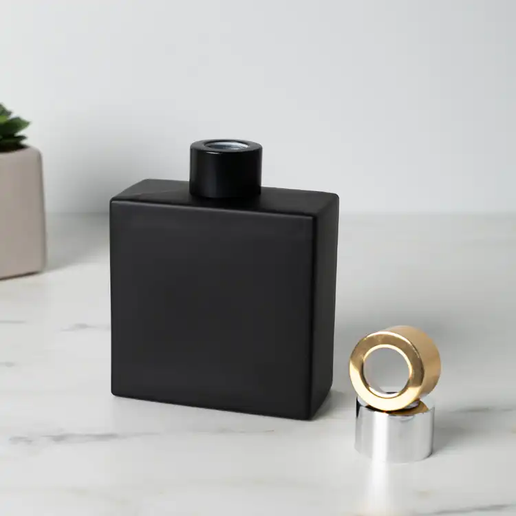 Matte Black Square Reed Diffuser Bottle with Matte Black Reed Diffuser Collar on table next to Silver and Gold Reed Diffuser Collar