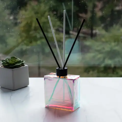 Prism Square Reed Diffuser Bottle with Matte Black Reed Diffuser Collar and Fiber Diffuser Reeds in front of window
