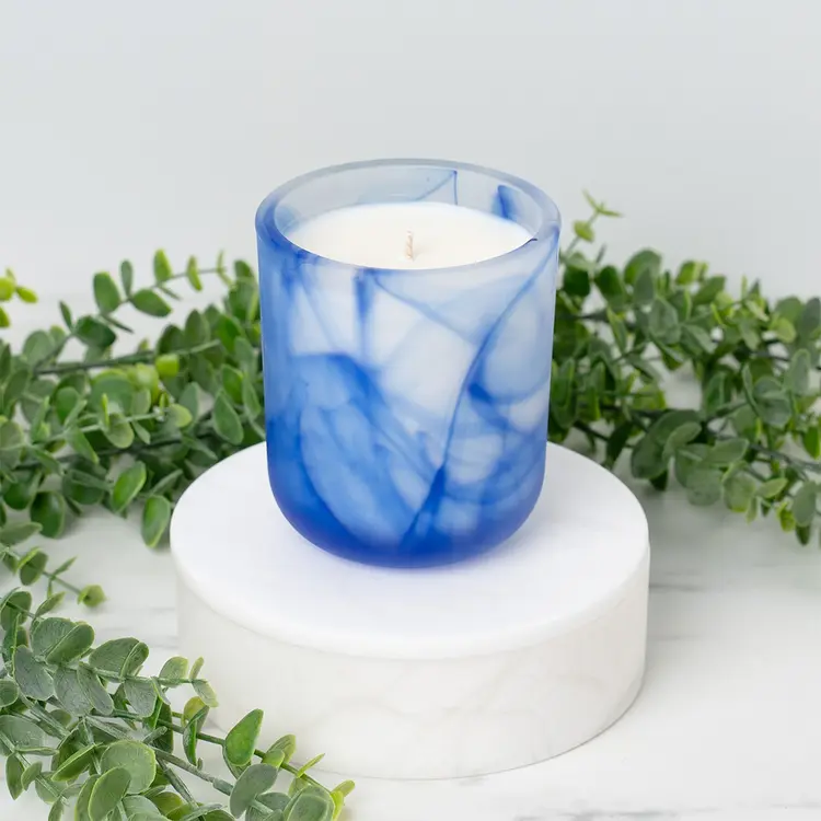 Frosted Blue Swirl Sonoma Tumbler Jar candle in front of greenery
