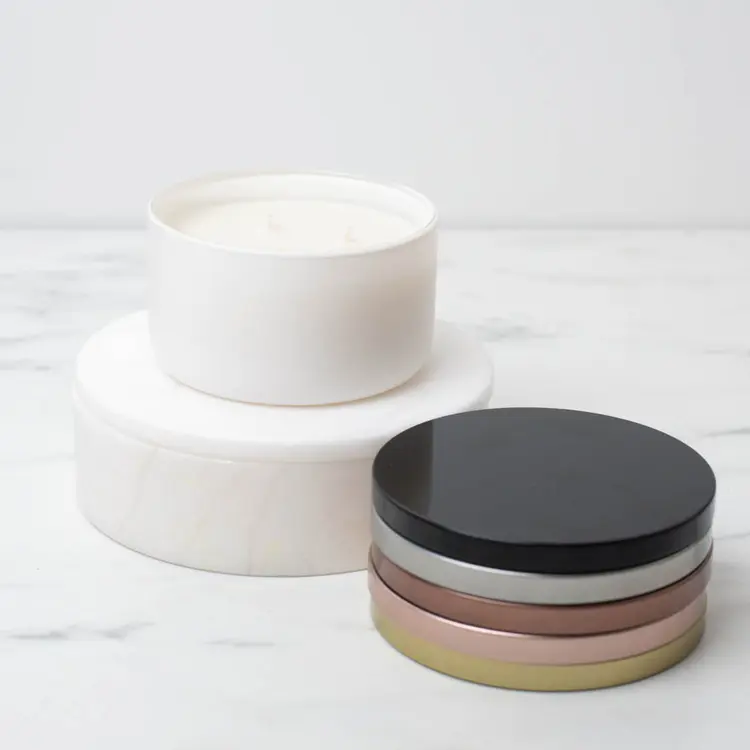 Matte White Calista Tumbler Jar on a white riser with metal flat lids stacked beside it.