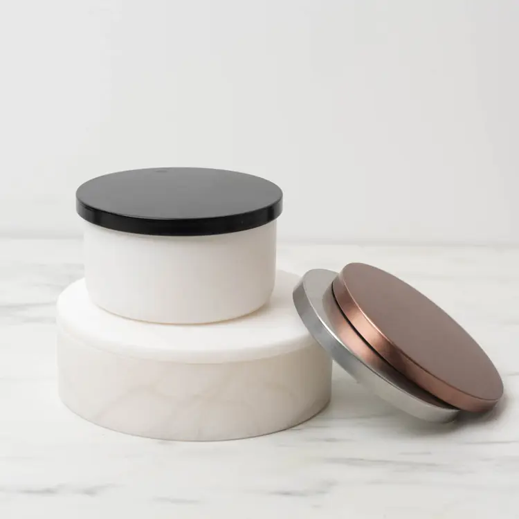 Matte White Calista Tumbler Jar with Black Metal Flat Lid on a white riser with metal flat lids stacked beside it.
