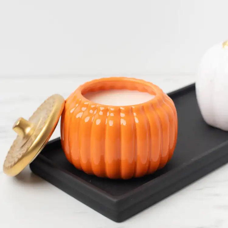 Harvest Orange Ceramic Pumpkin Jar with Gold Matte Lid on its side on a black wooden tray