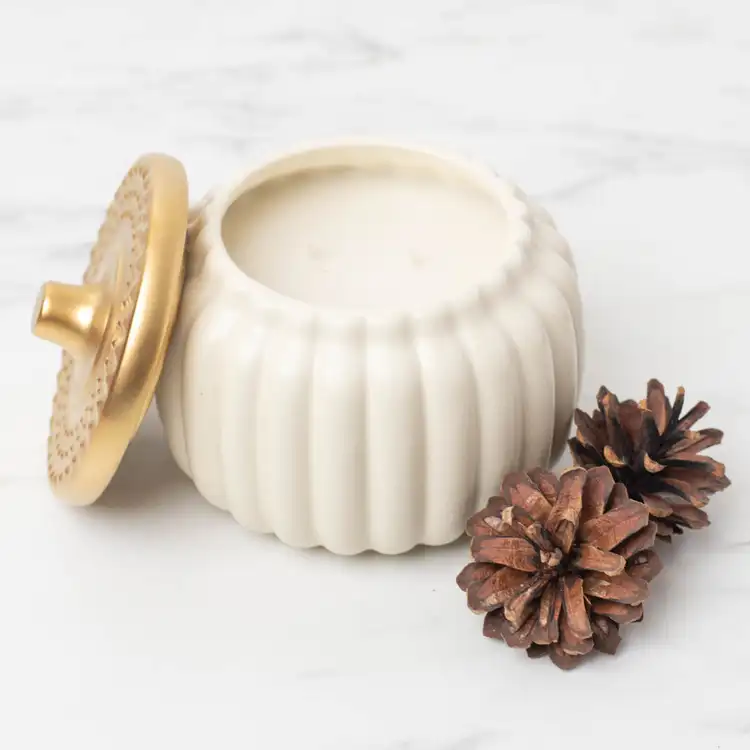 Harvest Ivory Ceramic Pumpkin Jar with Gold Matte Lid on a marble countertop with a pine cone