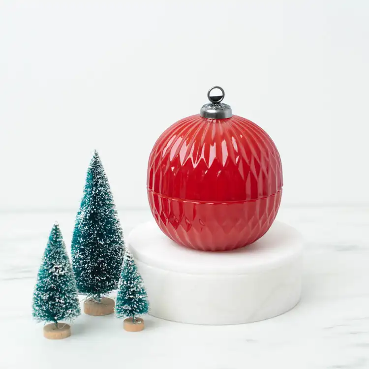 Red Glass Ornament Jar on a white pedestal and marble countertop with ornamental pine trees 