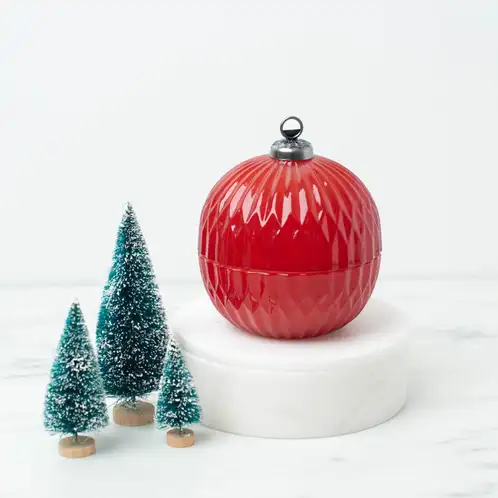 Red Glass Ornament Jar on a white pedestal and marble countertop with ornamental pine trees