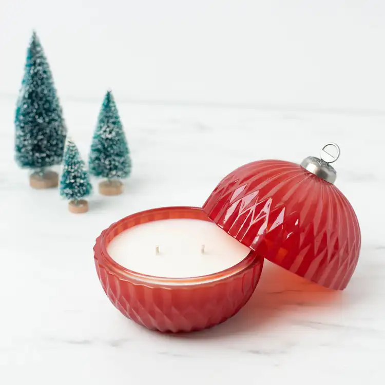 Red Glass Ornament Jar with lid half removed on a marble countertop with ornamental pine trees