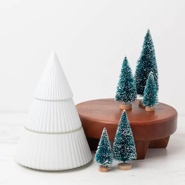 White Glass Tree Jar on a marble countertop with decorative pine trees on a wooden base.