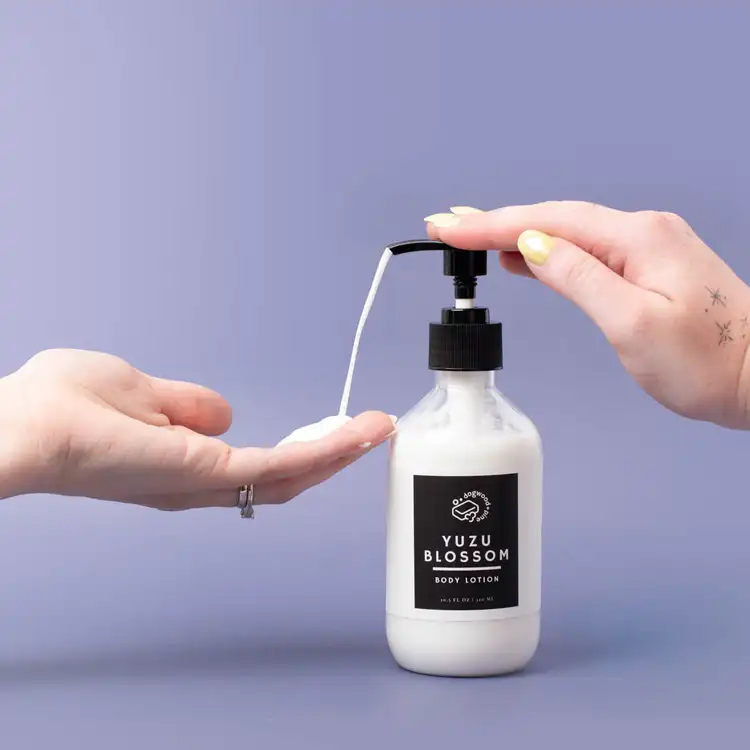 A hand pumping a finished lotion base in elegant packaging out of the bottle on a purple background
