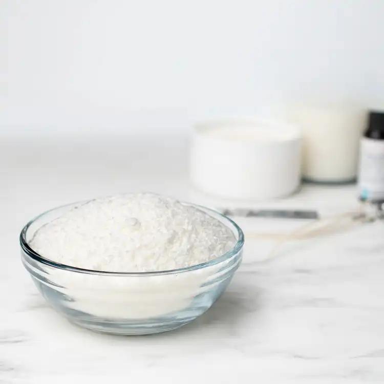 A glass bowl of granular SimplySoy wax on a white marble countertop. 