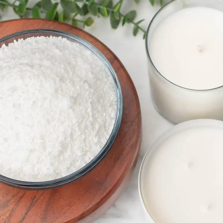 A bowl of granular SimplySoy wax on a wooden riser beside to finished candles. 
