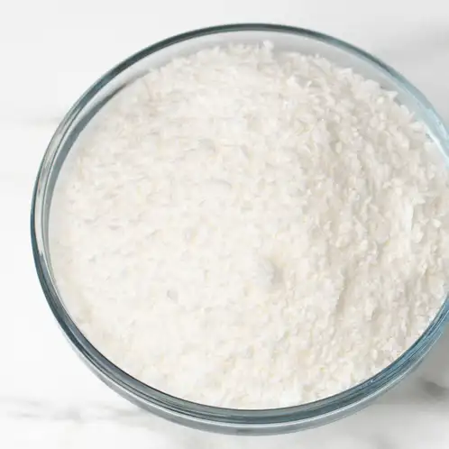 Looking down on a glass bowl of SimplySoy wax on a white marble countertop.