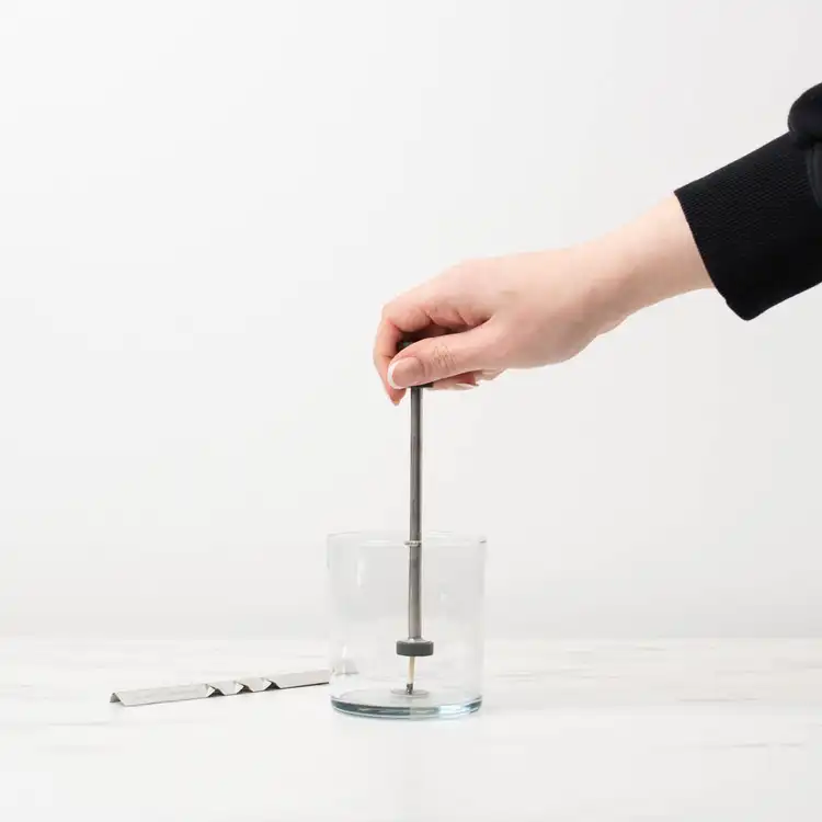 CandleScience Small Single Wick Setter pulling away from a clear straight sided tumbler jar showing the wick staying behind.