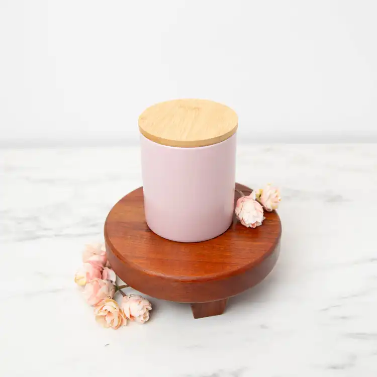 Blush Modern Ceramic Tumbler with a bamboo lid on a wooden pedestal with rose buds scattered around the container 