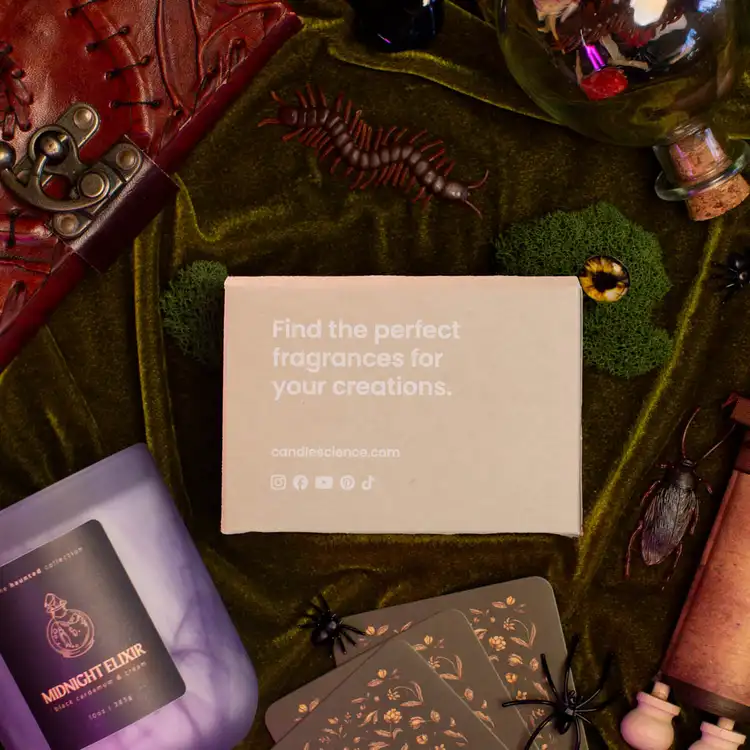 A kraft fragrance flight box that reads "find the perfect fragrances for your creations" surrounded by moss, a leather bound book, corked bottles, and icky bugs