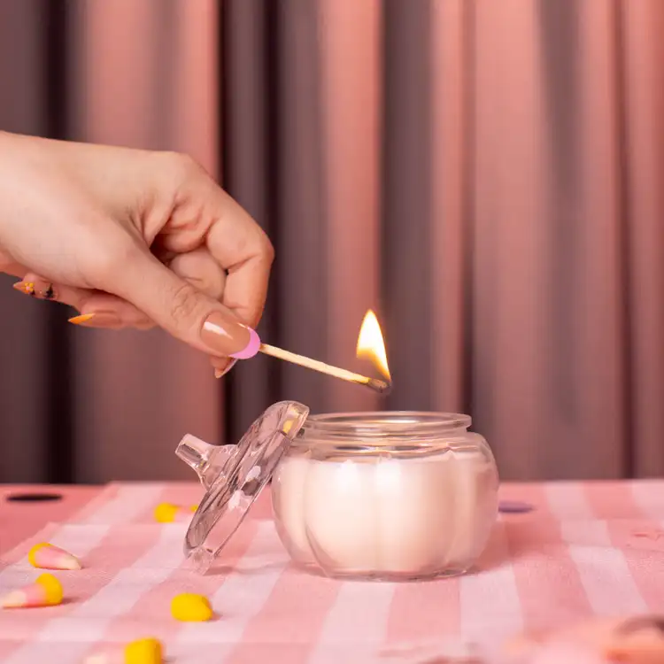 Mini Clear Glass Pumpkin Jar with a hand holding a match lighting the candle