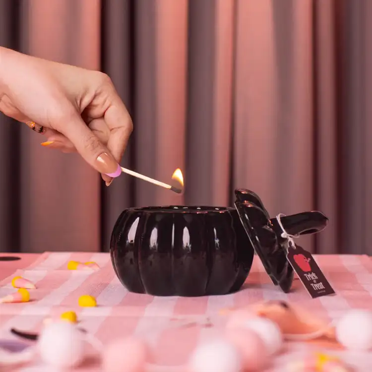 Black Ceramic Stemmed Pumpkin Jar with a hand holding a match lighting the candle