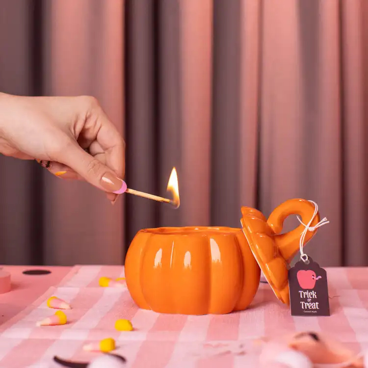 Orange Ceramic Stemmed Pumpkin Jar with a hand holding a match lighting the candle
