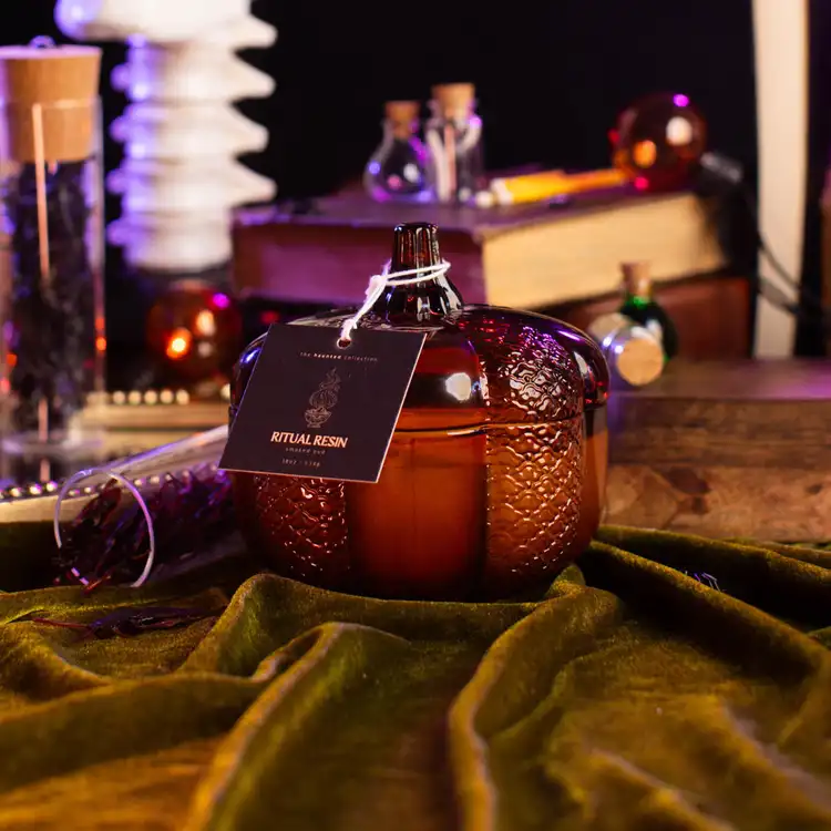 Amber Heirloom Glass Pumpkin Jar with a hang tag filled with a candle in a gothic setting