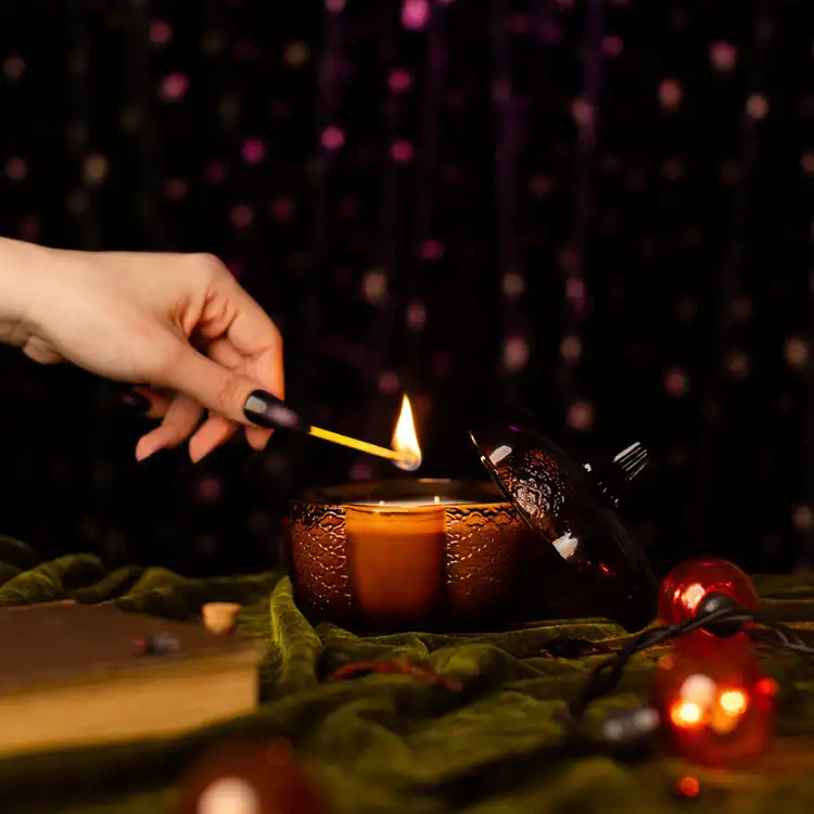 Amber Heirloom Glass Pumpkin Jar filled with a candle in a gothic setting with a hand holding a match