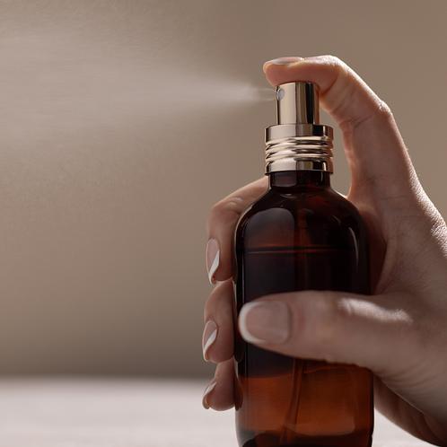 An elegant amber perfume bottle with a soft gold top spraying perfume
