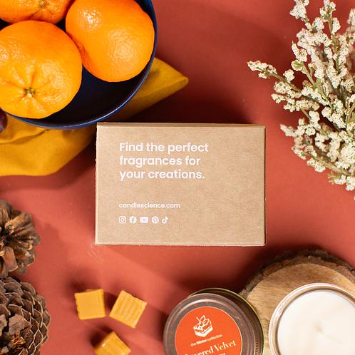 A kraft fragrance flight box on a warm, burnt sienna background with oranges, elderflower and caramels scattered. 